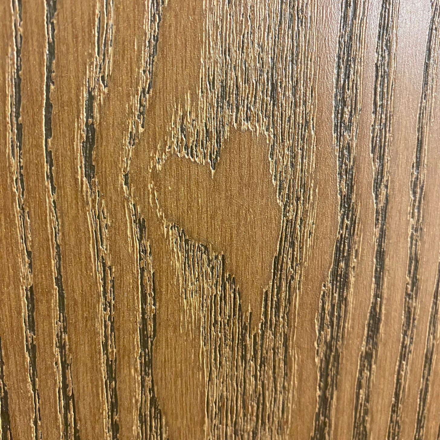 A heart etched into a piece of brown wood.