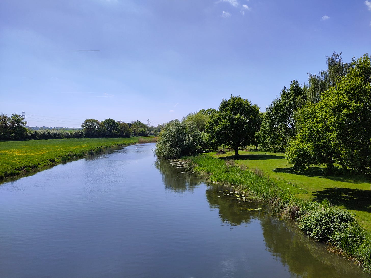 A wide calm river lined on both sides by meadows and trees. A wide calm river lined on both sides by meadows and trees.