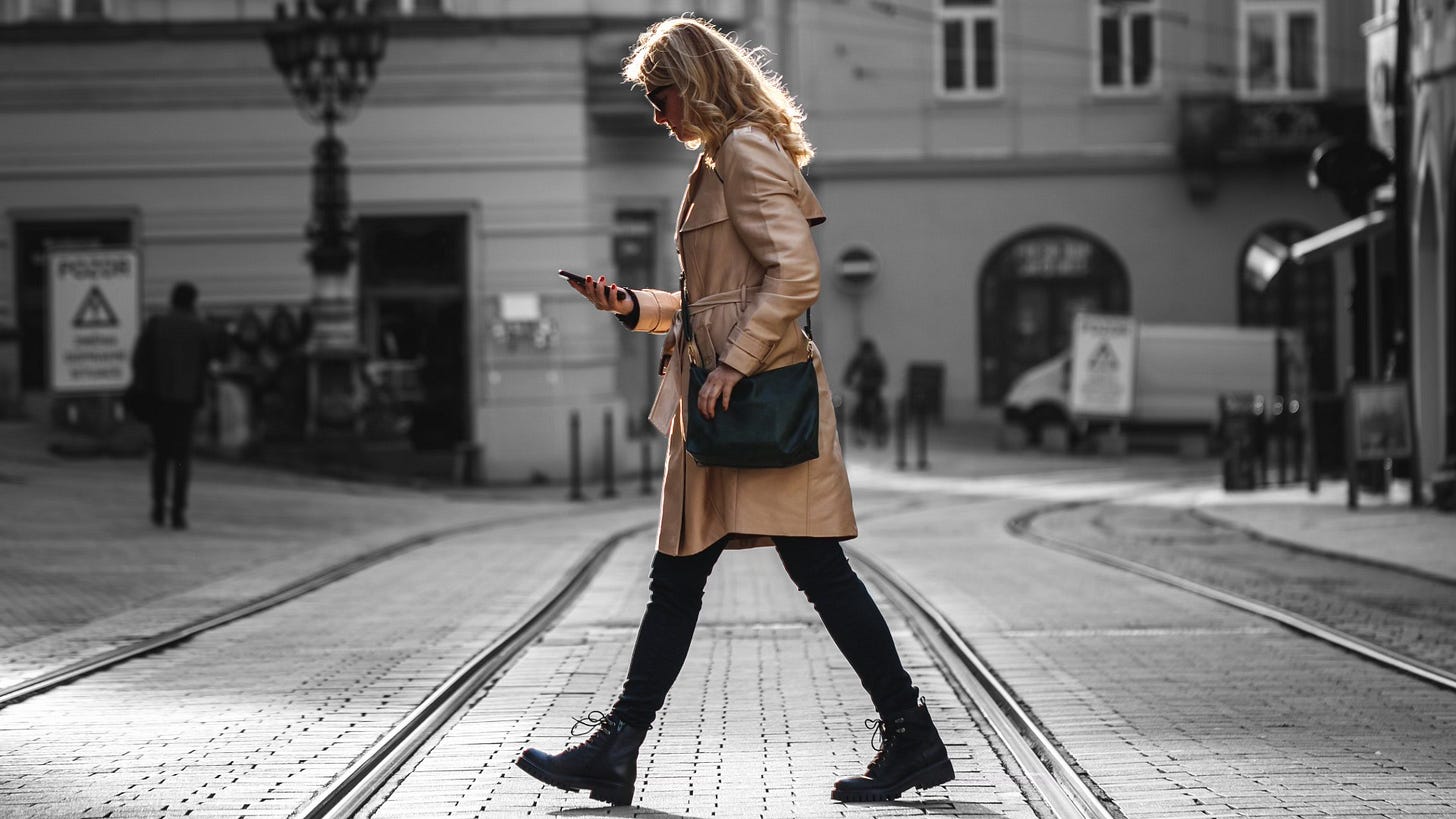 A woman looking at her mobile phone as she crosses the street A woman looking at her mobile phone as she crosses the street