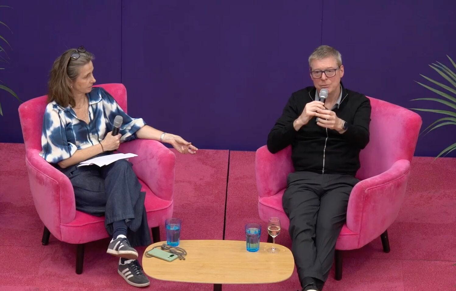 Amy Rennison, left, listens as Michael Barnard speaks into a microphone, both seated in vivid pink armchairs on matching pink carpet against a deep purple backdrop at Octopus Energy’s London headquarters. Amy Rennison, left, listens as Michael Barnard speaks into a microphone, both seated in vivid pink armchairs on matching pink carpet against a deep purple backdrop at Octopus Energy’s London headquarters.