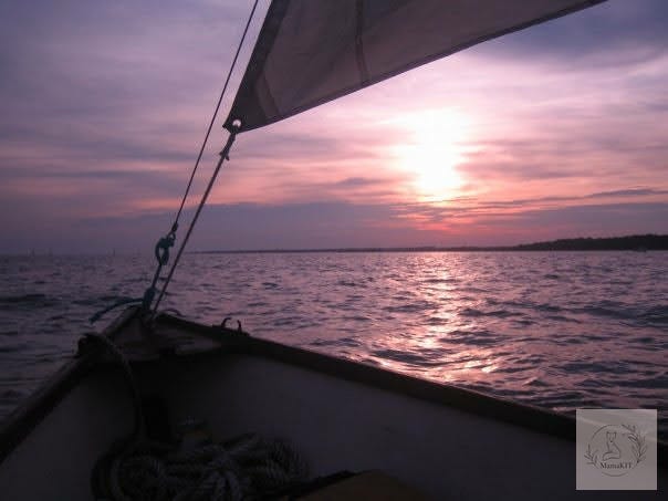 Sunset view from a sailboat—calm ocean waves and soft pink sky.