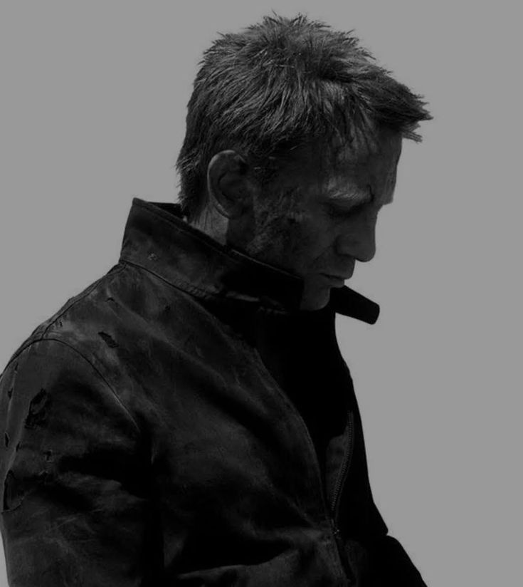 This may contain: a man in black leather jacket holding a cell phone and looking down at his face
