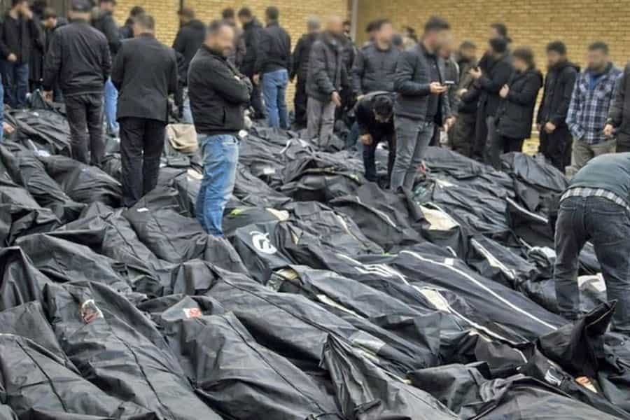 عده‌ای بالای پیکرهای کنار هم قرارگرفته‌ی جان‌باختگان کشتار اعتراضات ایستاده‌اند و در جست‌وجوی جسد عزیزان خود هستند.