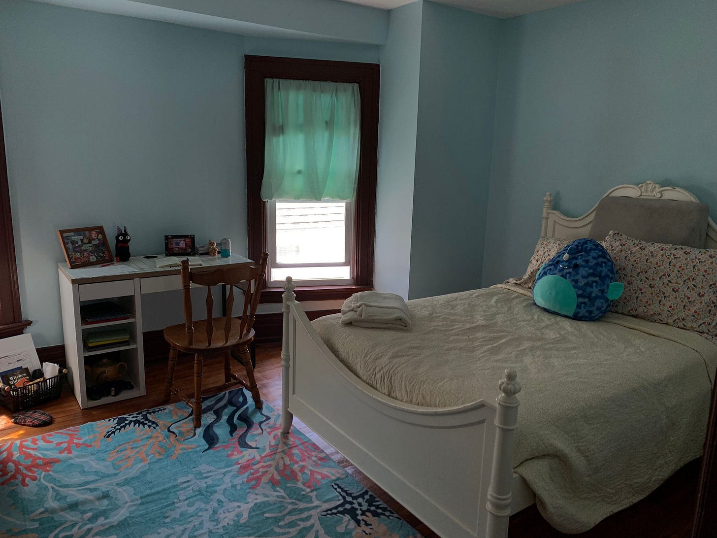 Image Description: Our guest bedroom / nursery, with light blue walls courtesy of Jo’s painting. Emory’s desk is against one wall, with a stuffed Jiji from Kiki’s Delivery Service and his collages framed on it. Our new rug, with a coral reef pattern, is spread out. 
