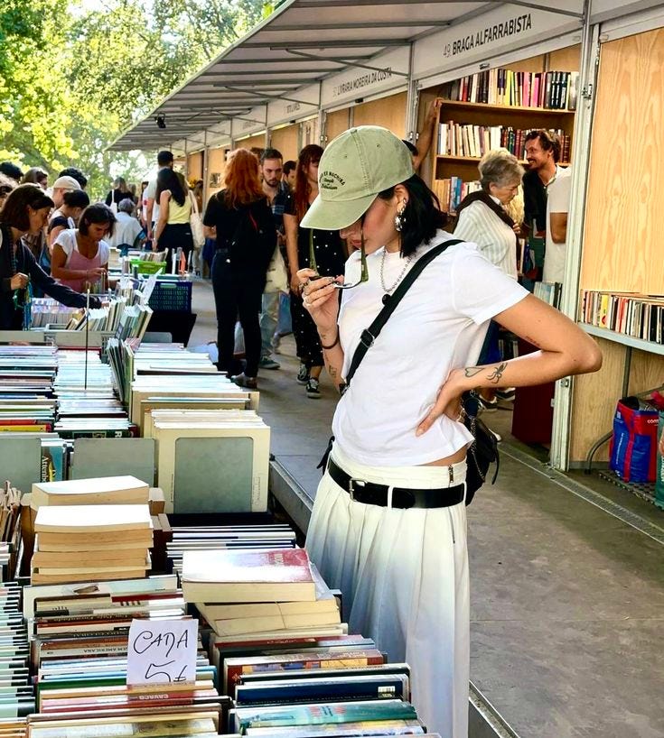This may contain: a woman standing in front of a book stand with lots of books on the table