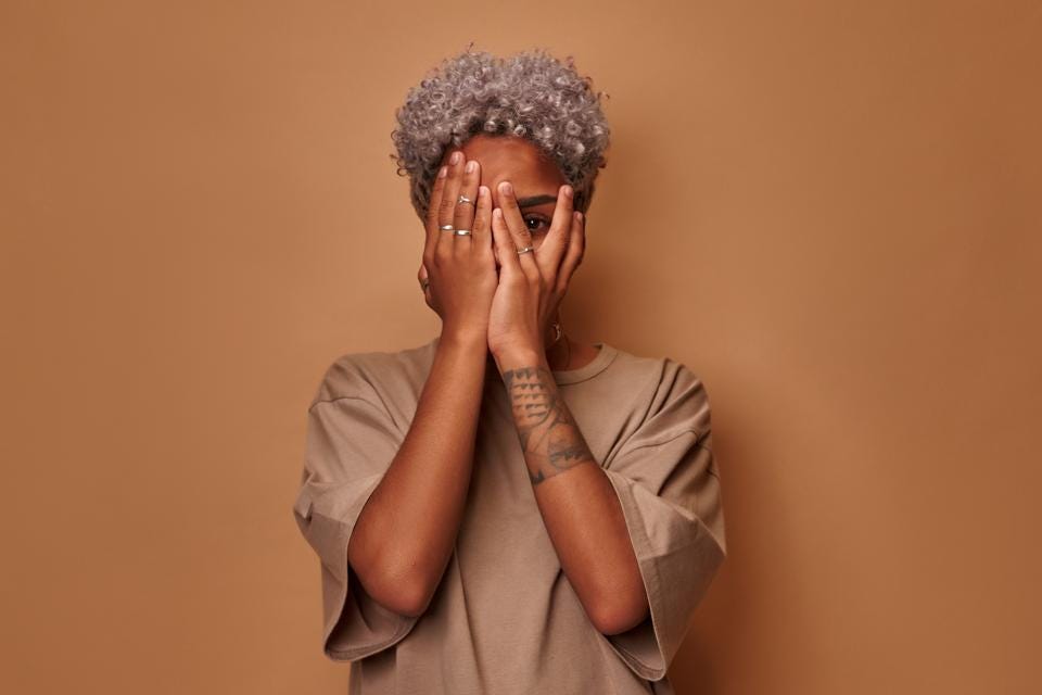 Frightened dark skinned woman covers face with palms peeks through fingers Frightened dark skinned woman covers face with palms peeks through fingers