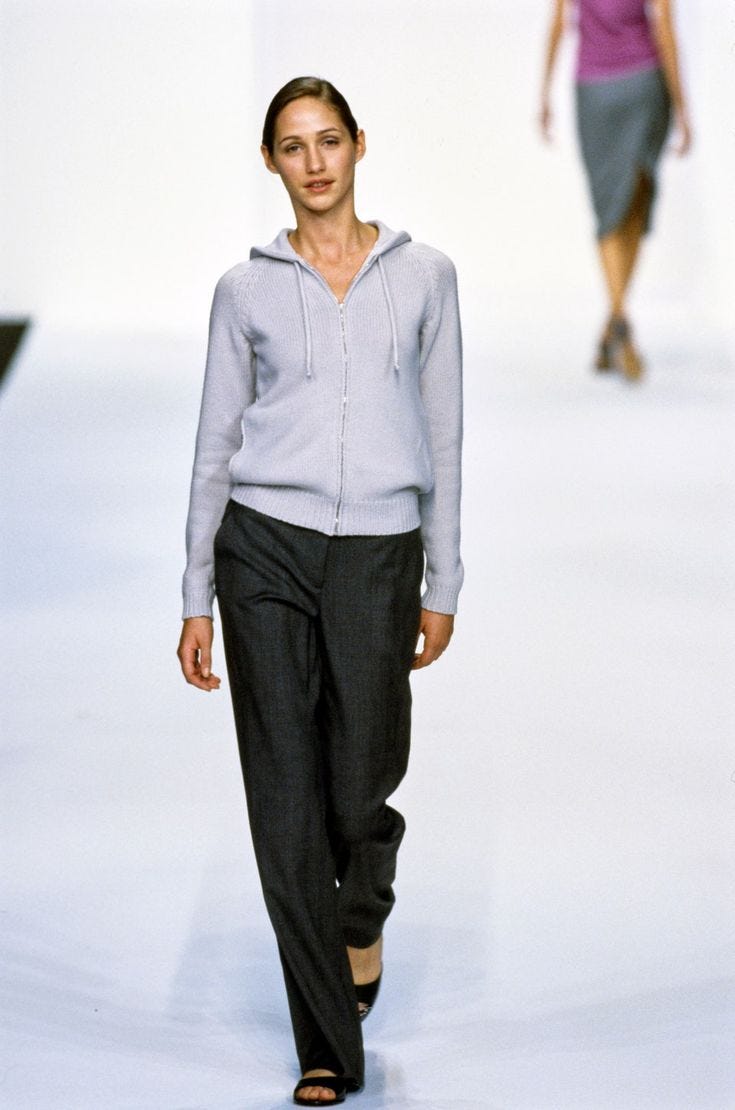 This may contain: a woman is walking down the runway wearing black pants and a hoodie sweater with an open back