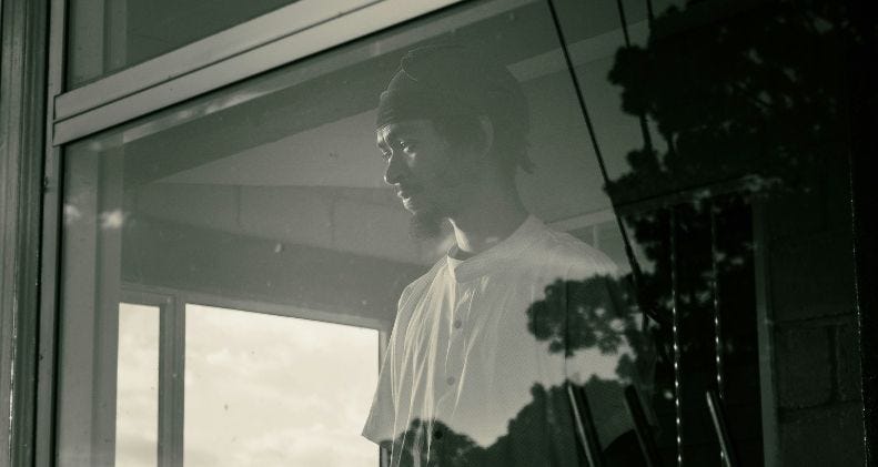 eine person, die vor einem fenster steht und nachdenklich nach draußen blickt. Foto von ALLAN LAINEZ auf Unsplash