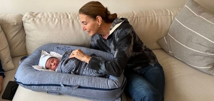 A woman seated on a couch, looking down at a newborn baby