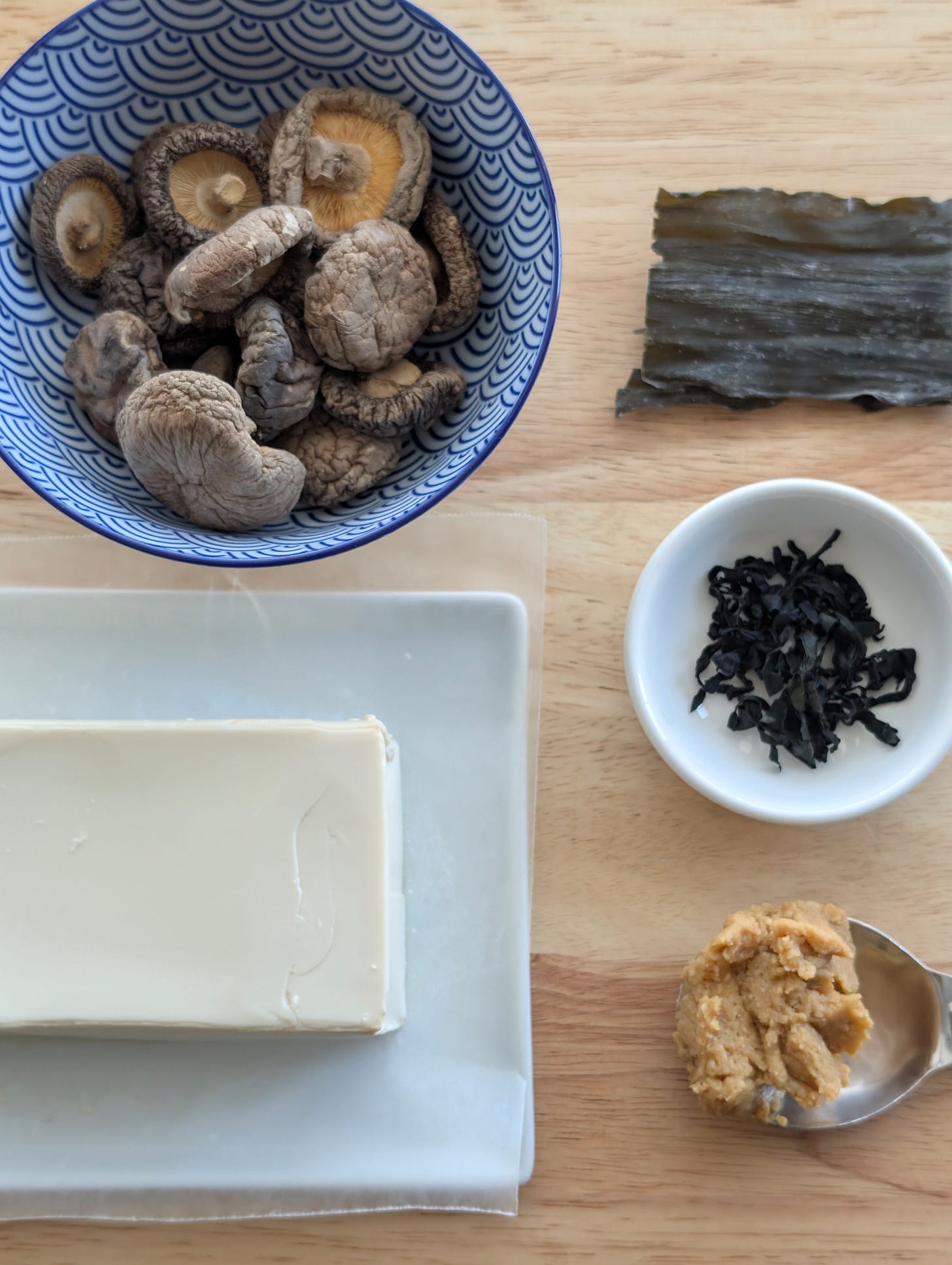 Ingredients for miso soup—miso paste, tofu, and shiitake mushrooms—arranged neatly on a wooden cutting board. Ingredients for miso soup—miso paste, tofu, and shiitake mushrooms—arranged neatly on a wooden cutting board.