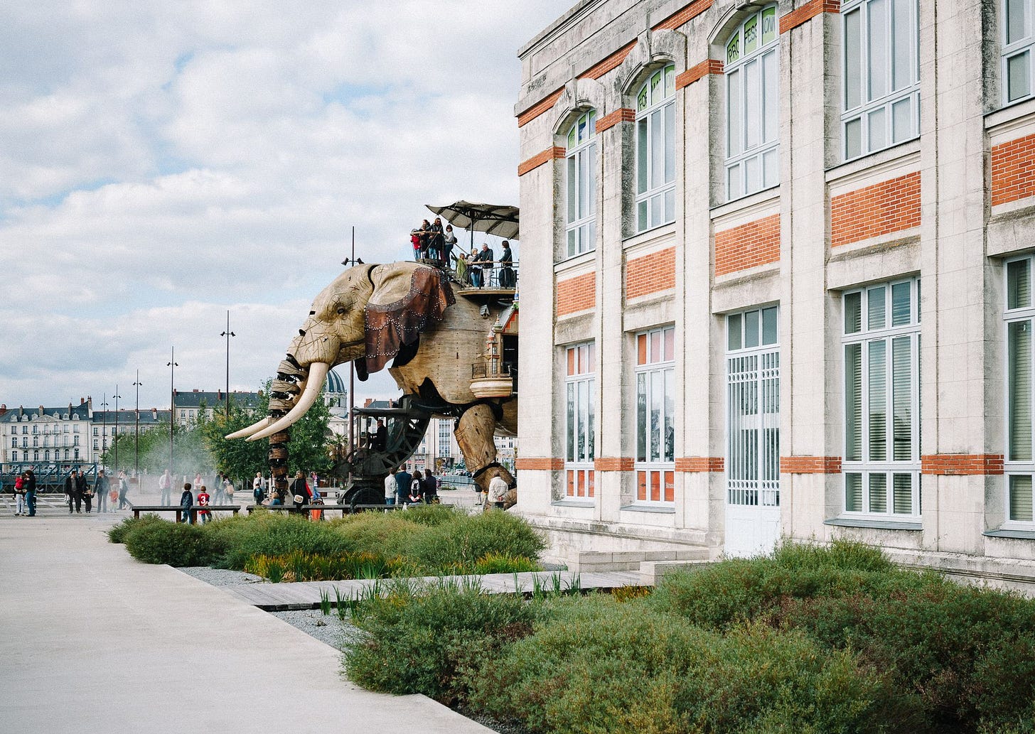 A giant wooden elephant carrying people walks around nice buildings in France.