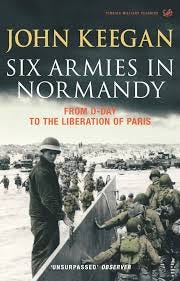 The cover is dominated by a landing craft discharging a long line of soldiers walking ashore. The sky above transitions from gray to black for the top 1/3rd of the cover. The author’s name is across the top in bold gold lettering, while the title appears in white text immediately below. Mid-page in smaller red font is the books’ subtitle “From D-Day to the Liberation of Paris.”  