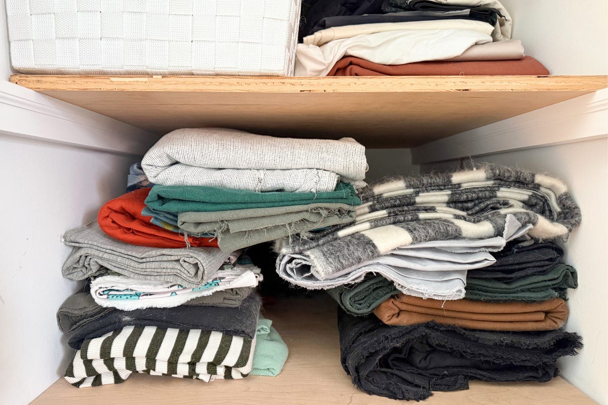 Neatly folded fabrics in neutral colors organized on white closet shelves with wooden shelves