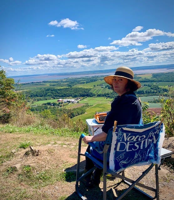 Photo one is a woman in a straw hat sitting with a typewriter overlooking a verdant valley below. Photo two is a bright orange typewriter sitting on a table with a valley in the distance