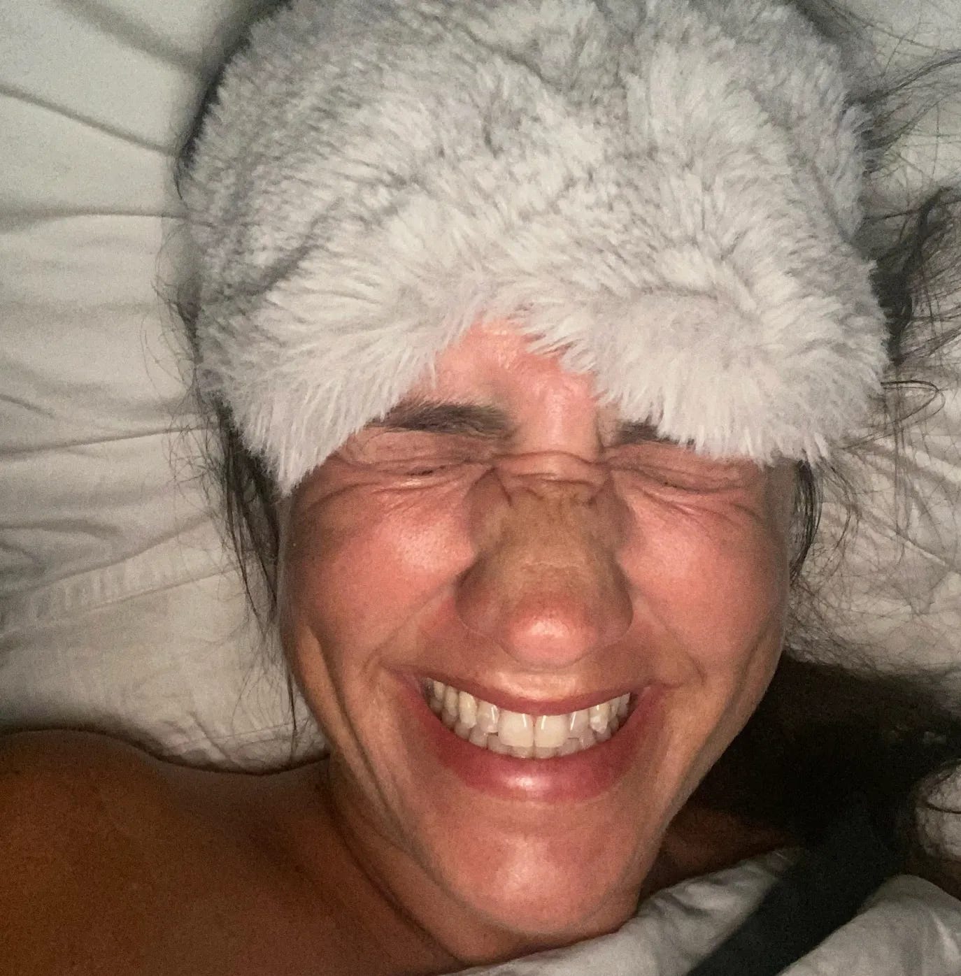 Donna Francis from The Beauty Ed® smiling broadly in bed, wearing a thick faux-fur headband and capturing the "back to school" feeling of a New Year Monday.