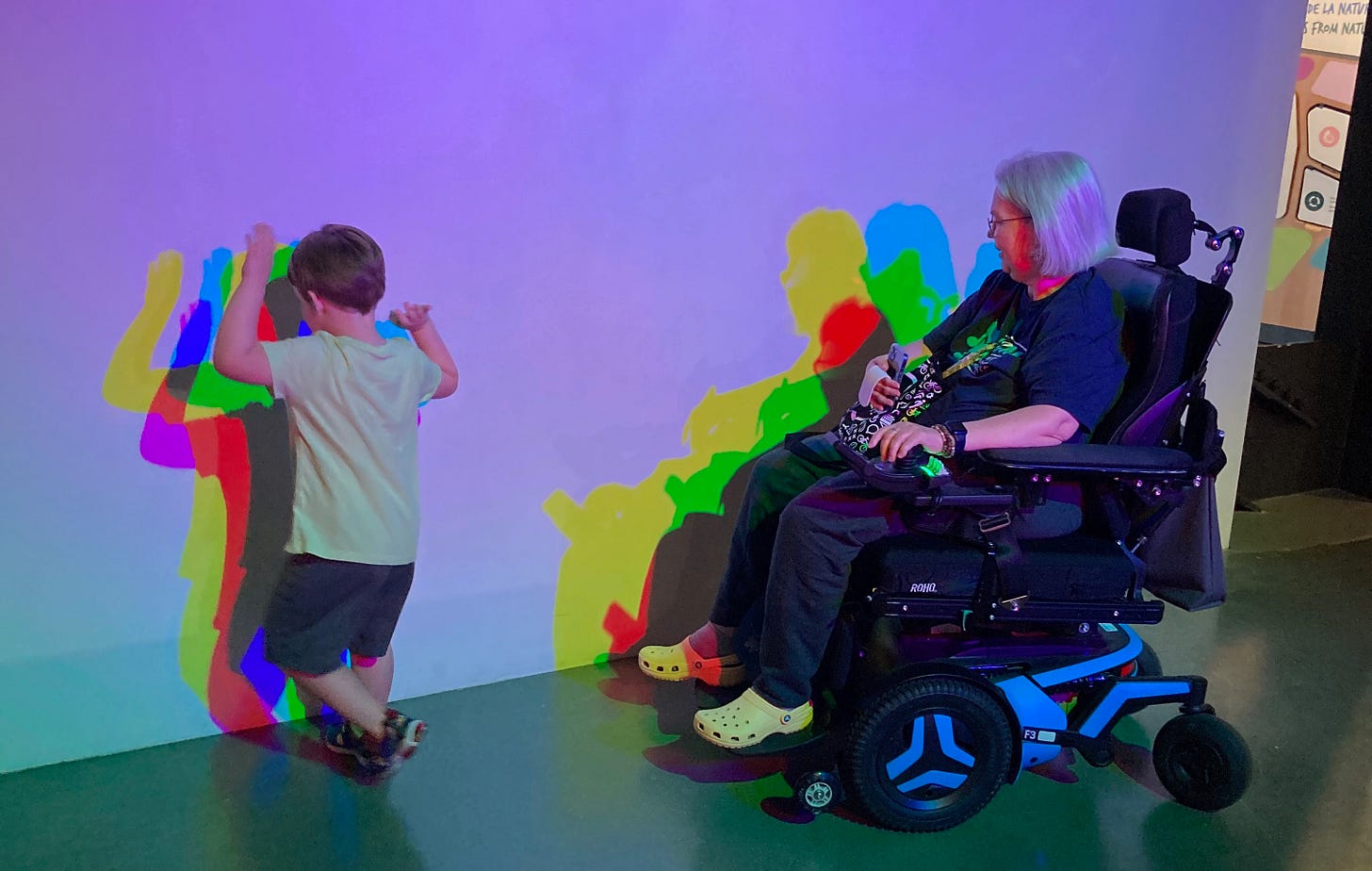 Me and my wheelchair and a four year-old and a T-shirt and shorts, both with colorful shadows from the science museum