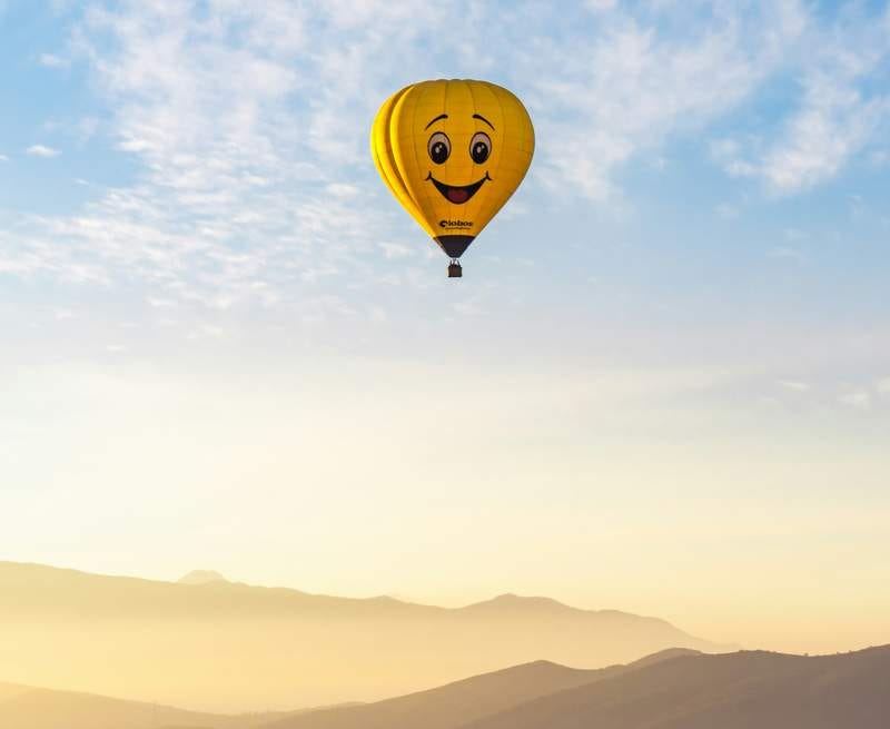 Photo of hot air baloon with a smiley face on it floating against a blue sky.