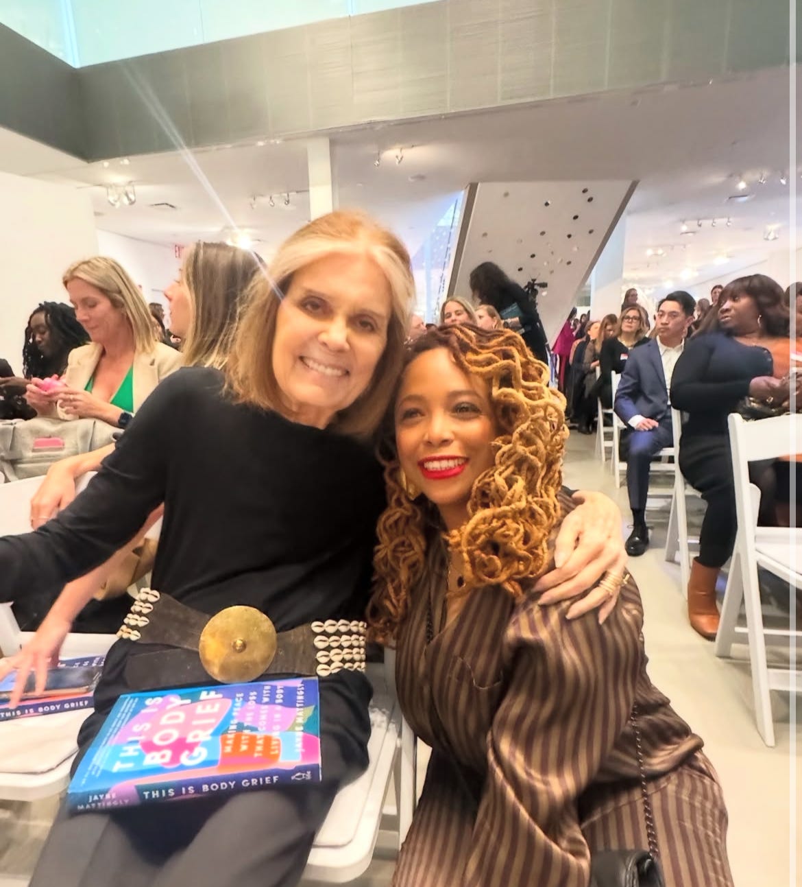 Gloria Steinem and Dr. Nola Haynes posing for a photo with THIS IS BODY GRIEF by Jayne Mattingly in Gloria Steinem's lap