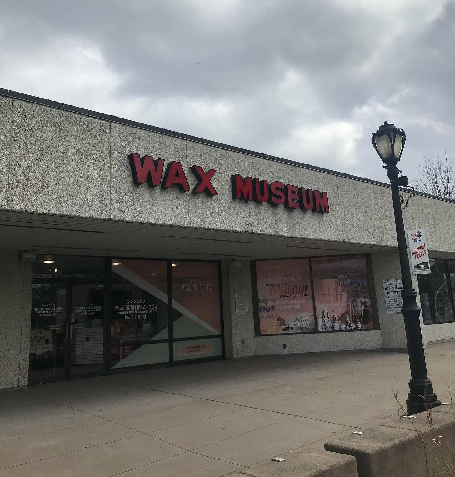 A photo of the exterior of the Niagara Falls historical wax museum on a day with grey dreary weather. The museum has a grey pebble-dash exterior, a few windows and an old red sign saying 'wax museum'.