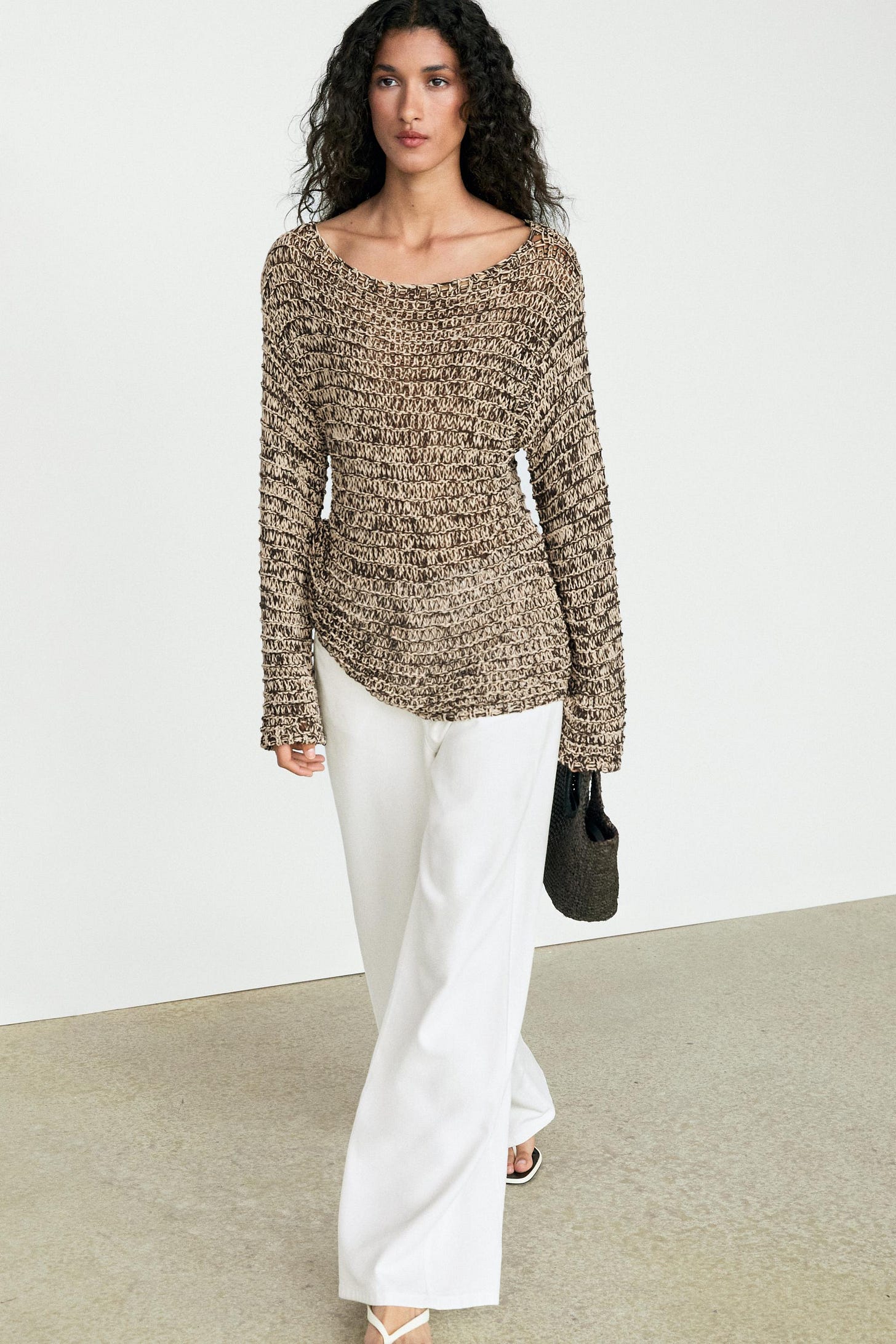 Ensemble composé d'un pull couleur sable en maille ouverte chinée, à encolure bateau et manches longues, et d'un pantalon blanc long à jambes larges.
