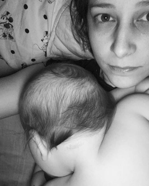 ID5: A black and white photo of the author Olivia Dreisinger. She is laying in what looks a bed with her child laying across her chest. It is a selfie. 
