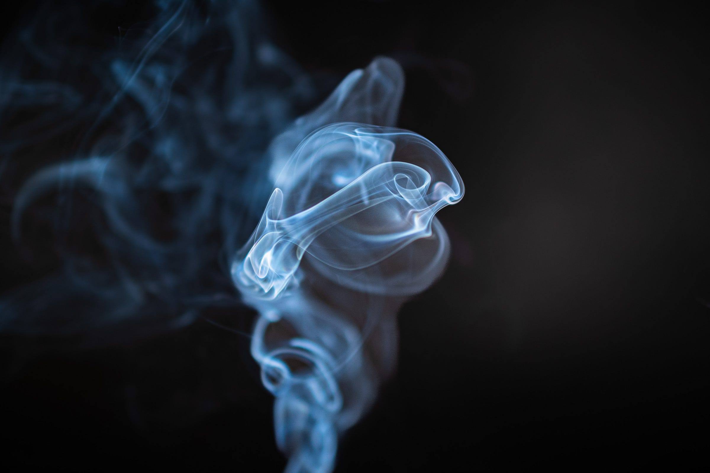 Blue smoke spirals upward against a black background. The image resembles a figure holding a stringed instrument