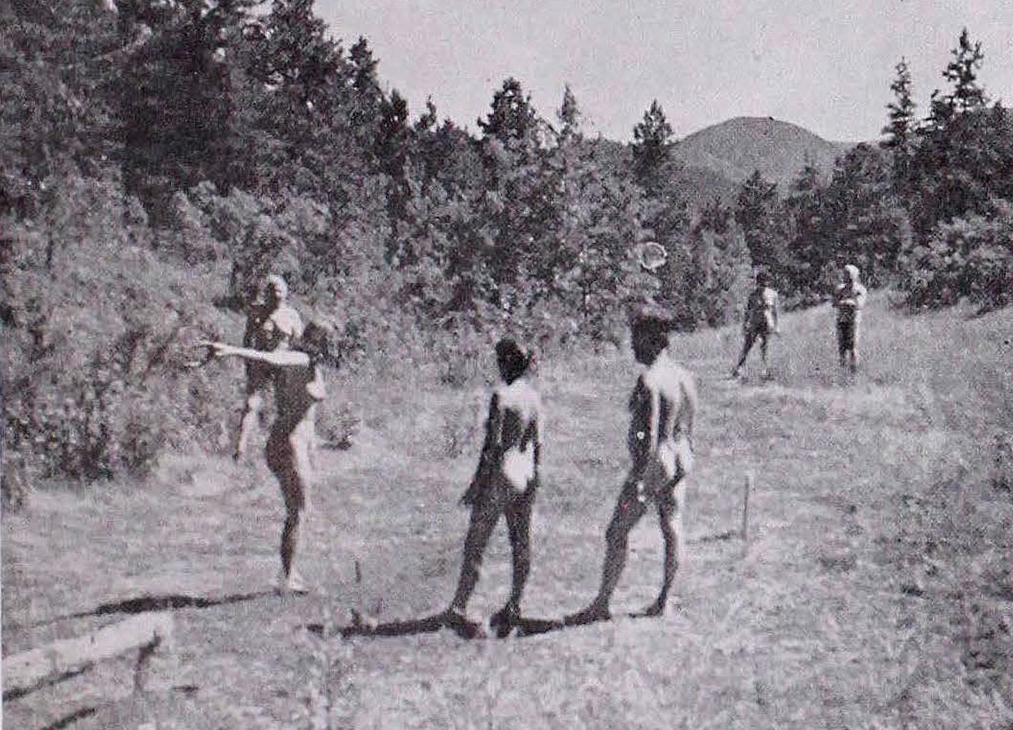 Black-and-white photo of nude Colorado Sunshine Club members playing horseshoes in a grassy, wooded area surrounded by pine trees, with a mountain peak visible in the distance. Black-and-white photo of nude Colorado Sunshine Club members playing horseshoes in a grassy, wooded area surrounded by pine trees, with a mountain peak visible in the distance.