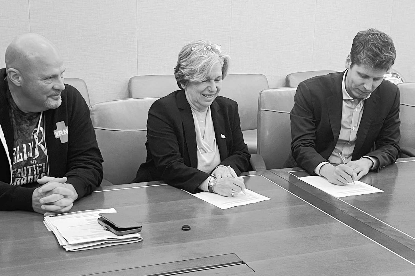 Three individuals signing documents at a formal meeting, likely related to the launch of the AFT National Academy for AI Instruction in New York Three individuals signing documents at a formal meeting, likely related to the launch of the AFT National Academy for AI Instruction in New York