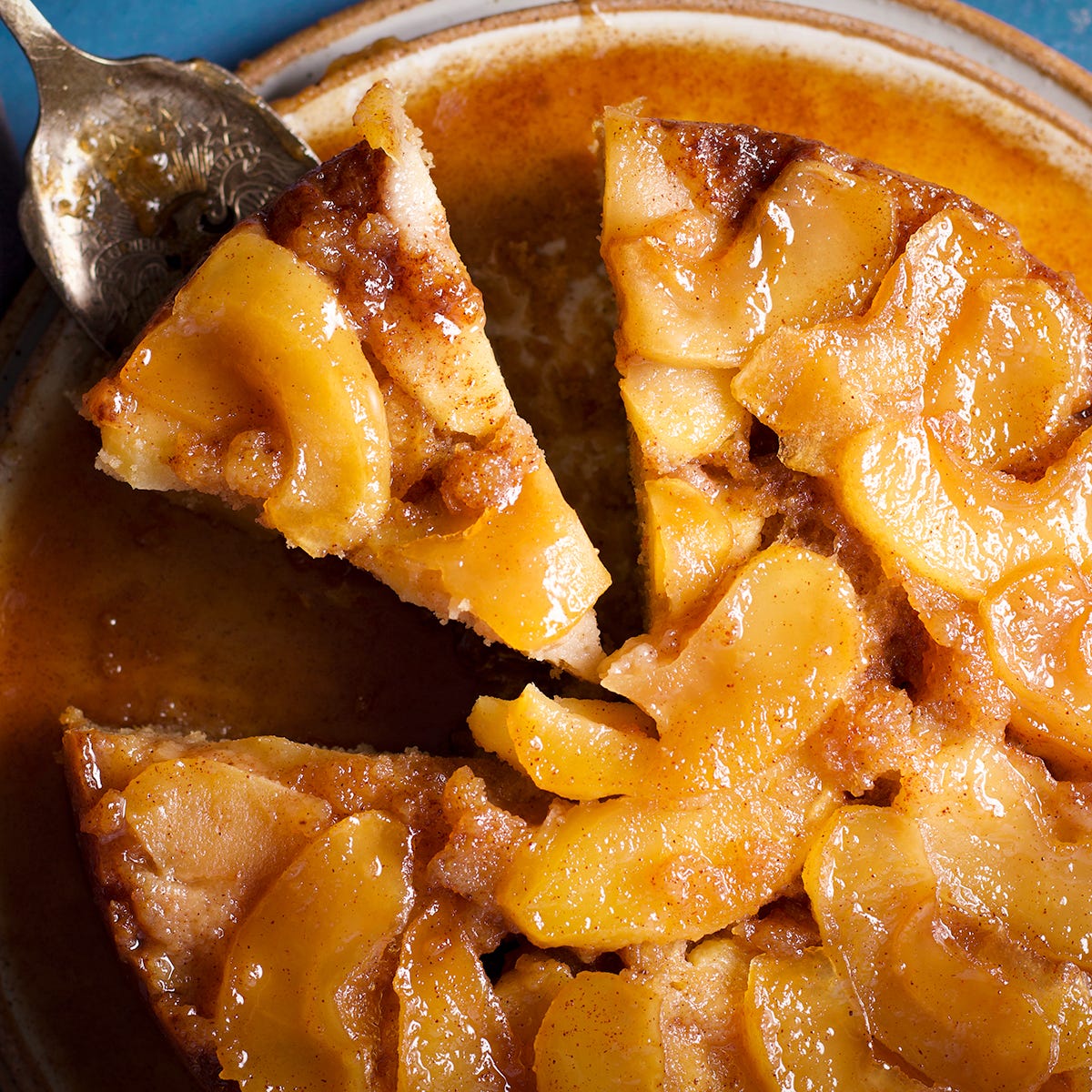 Someone using a cake server to remove a slice of apple upside down cake from the whole cake. Someone using a cake server to remove a slice of apple upside down cake from the whole cake.