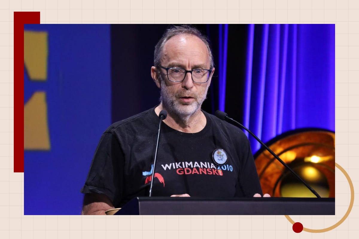 Jimmy Wales speaks at a podium wearing a black t-shirt from Wikimania 2010 Gdańsk, with a blue curtain behind him. Jimmy Wales speaks at a podium wearing a black t-shirt from Wikimania 2010 Gdańsk, with a blue curtain behind him.