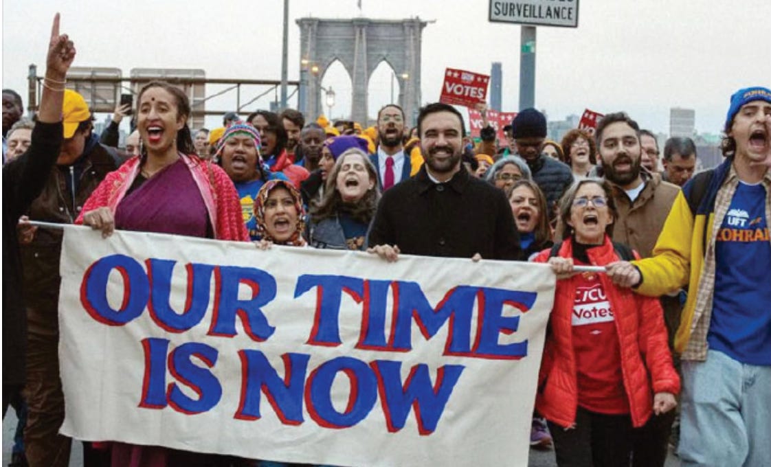 Mamdani and crowd of New Yorkers marching over Brooklyn bridge, carrying a banner that reads, "our time is now." 