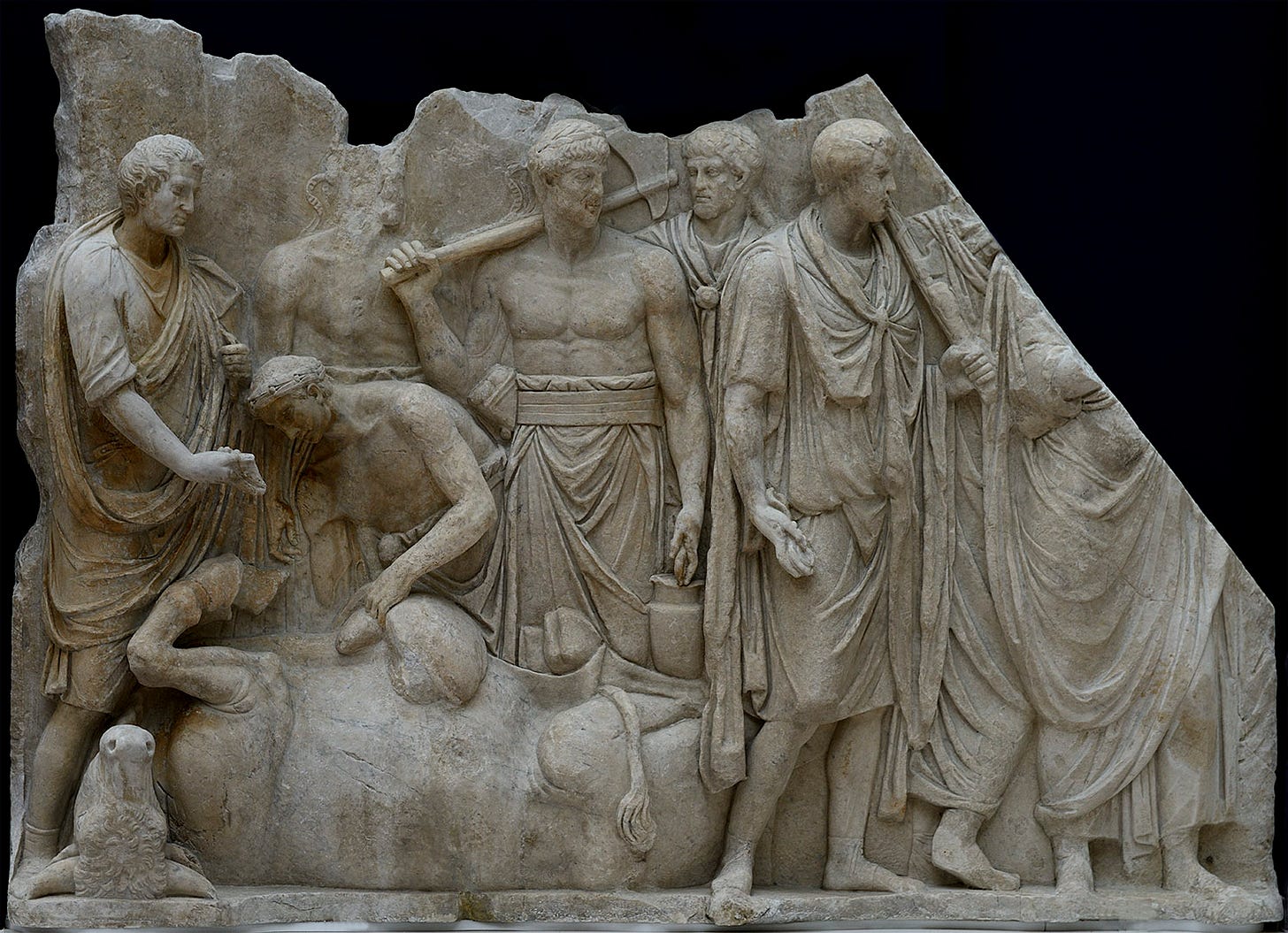 Foto do painel esquerdo do relevo de mármore "Sacrifício na frente do Templo de Júpiter Capitolino". Vários homens estão em pé, reunidos ao redor de um touro abatido, sacrificado, deitado no chão com as patas para o alto. Um sacerdote agachado se debruça sobre o touro e observa um órgão exposto na mão de outra figura.