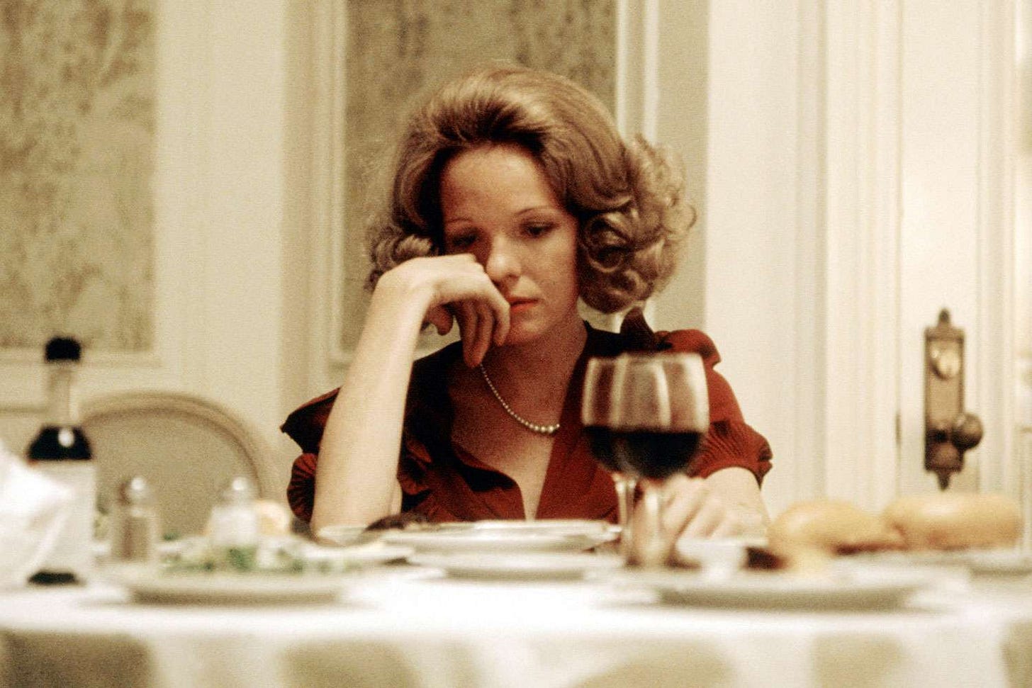Diane Keaton as Kay Adams sits at a table, looking somberly down at a table and wearing a red dress. Diane Keaton as Kay Adams sits at a table, looking somberly down at a table and wearing a red dress.