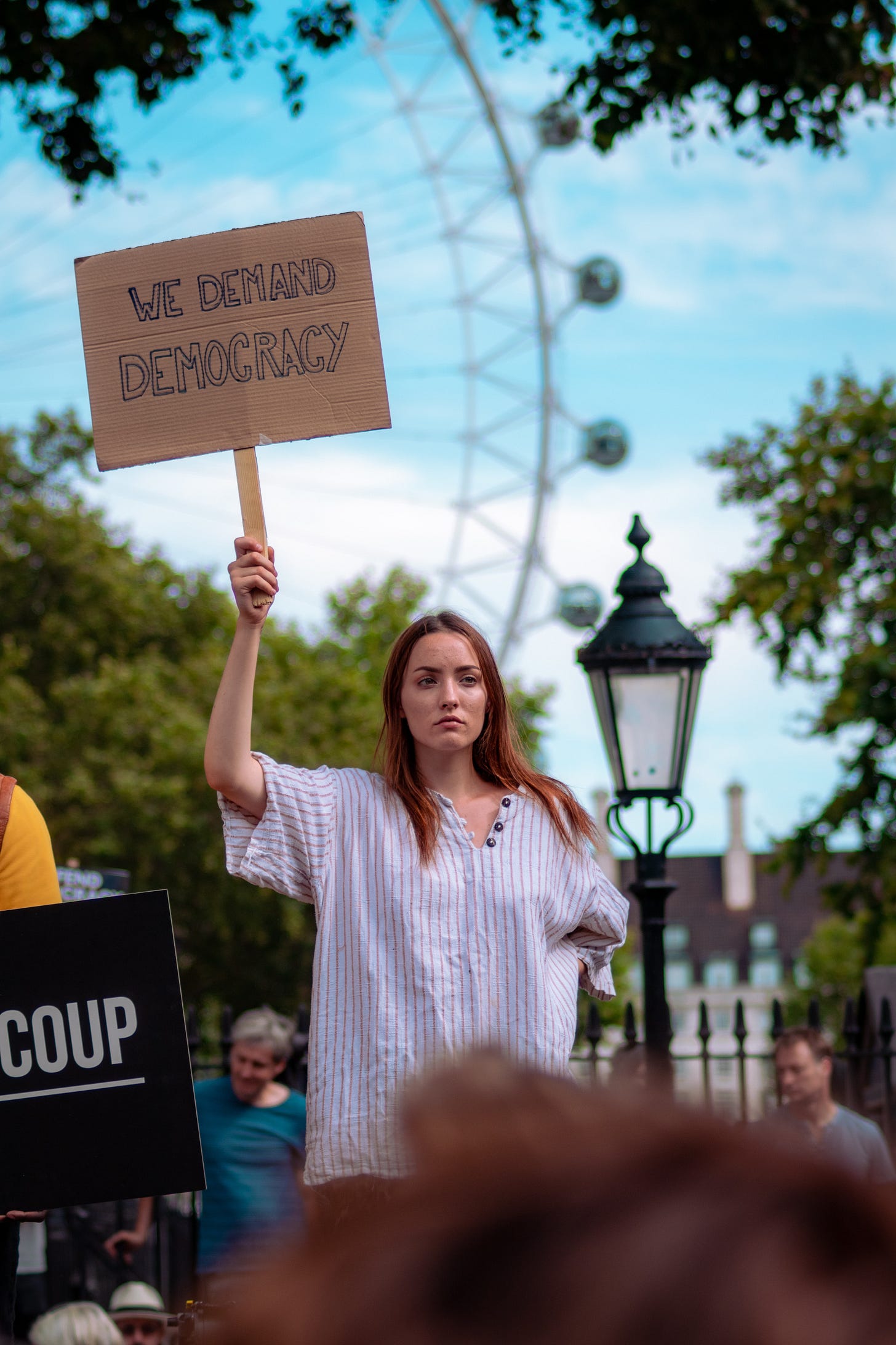 A photo of a young woman at a rally in London with a sign demanding democracy