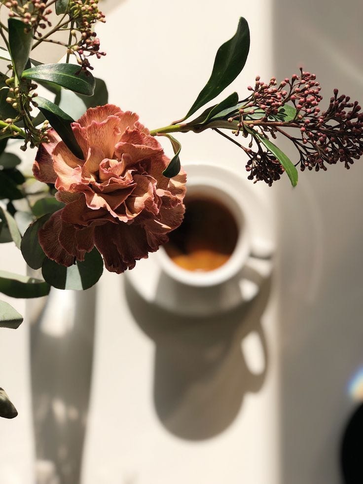 This may contain: a cup of coffee and some flowers on a table This may contain: a cup of coffee and some flowers on a table