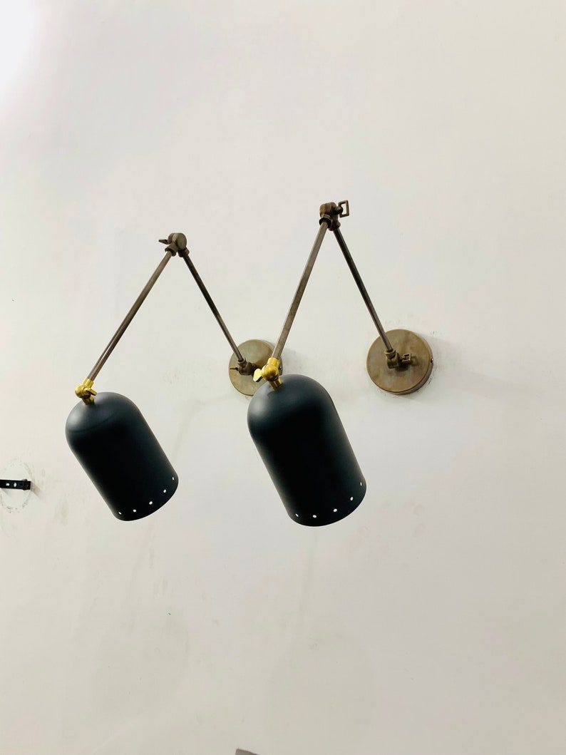 May include: Two black wall mounted lights with adjustable arms and a black shade with small holes. The lights are mounted on a white wall.