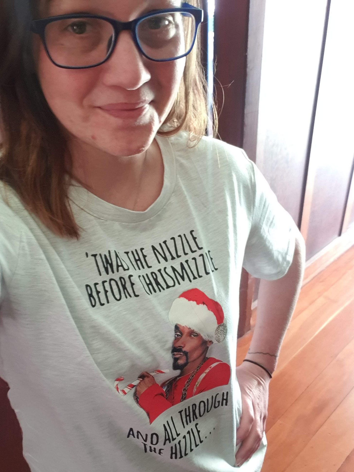 Charlotte has dark hair and glasses on and is wearing a t-shirt of Snoop Dogg in a Santa costume looking like he's smoking a candy cane.