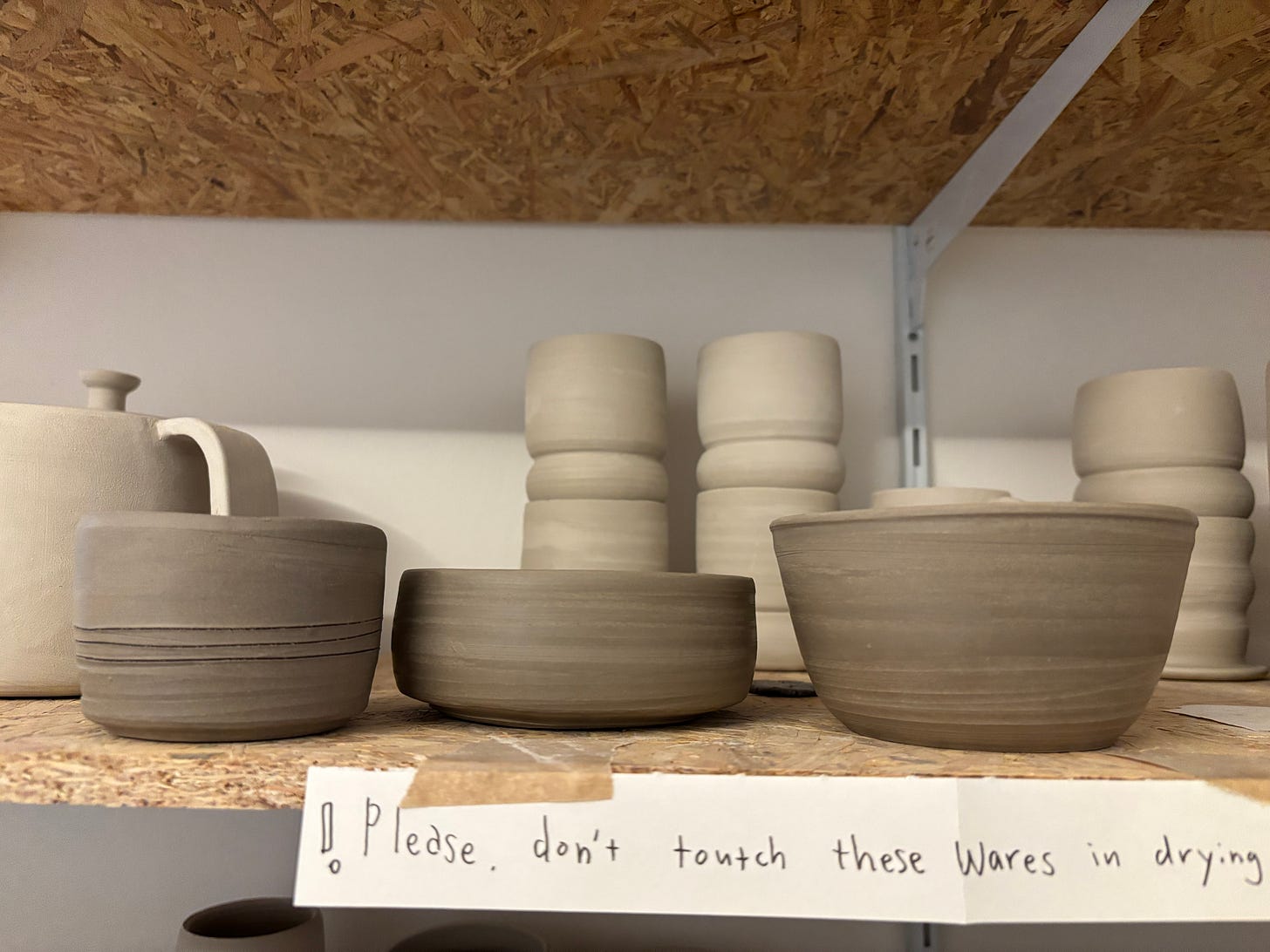 a plywood shelf topped with drying pottery - three small bowls in the foreground, with teapots and cups in the background