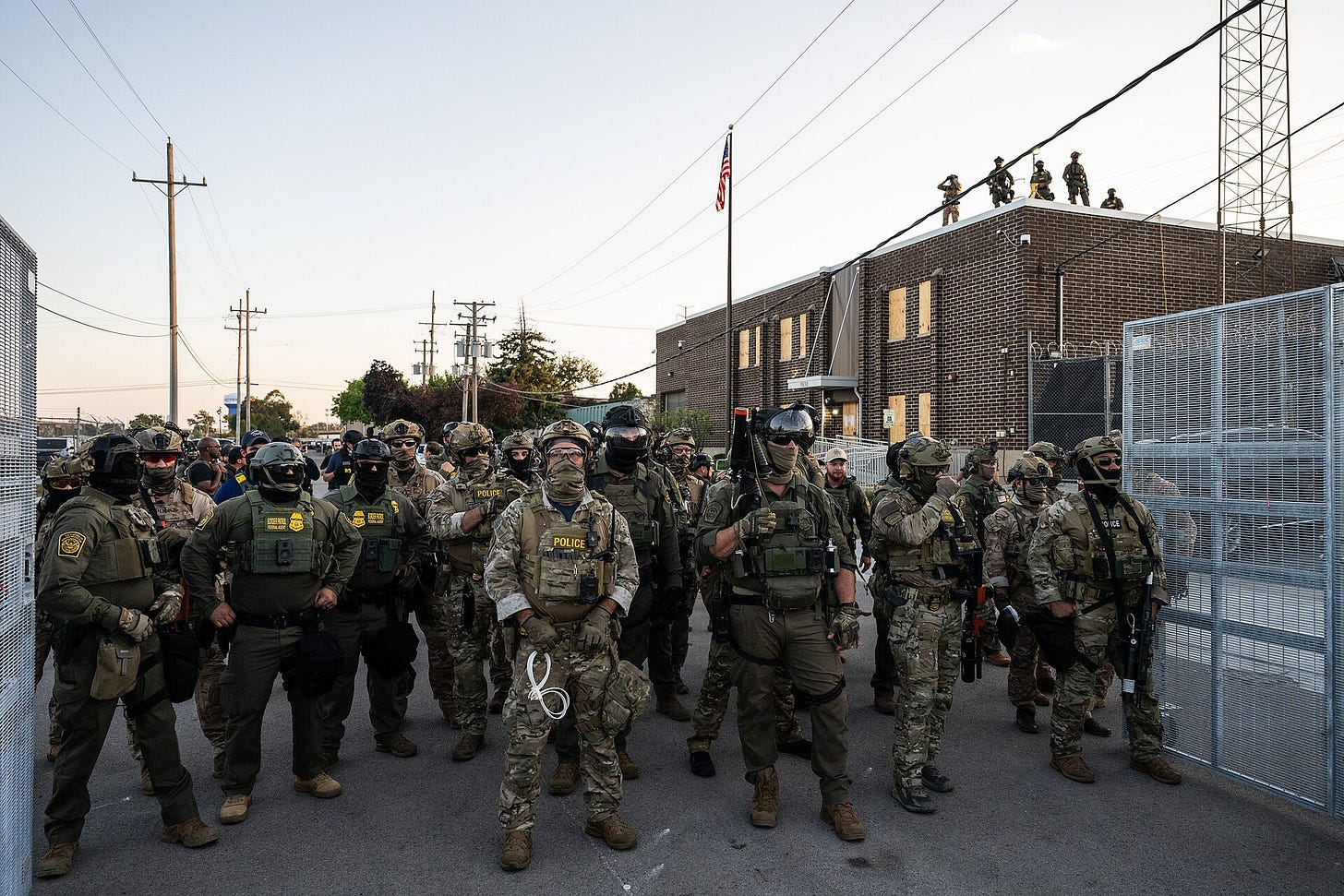 Sept 2025 pic of Broadview Ice Facility in Broadview IL; many ICE agents stand in gate wearing fatigues and masks and helmets; off to the side more agents stand on a roof. A flag is in the distance on a flagpole. They look like a fascist gestapo. Sept 2025 pic of Broadview Ice Facility in Broadview IL; many ICE agents stand in gate wearing fatigues and masks and helmets; off to the side more agents stand on a roof. A flag is in the distance on a flagpole. They look like a fascist gestapo.