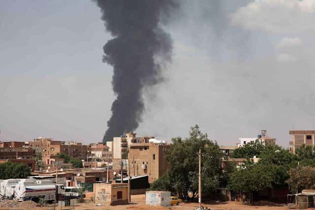 A thick plume of smoke rising in a column above a city. A thick plume of smoke rising in a column above a city.