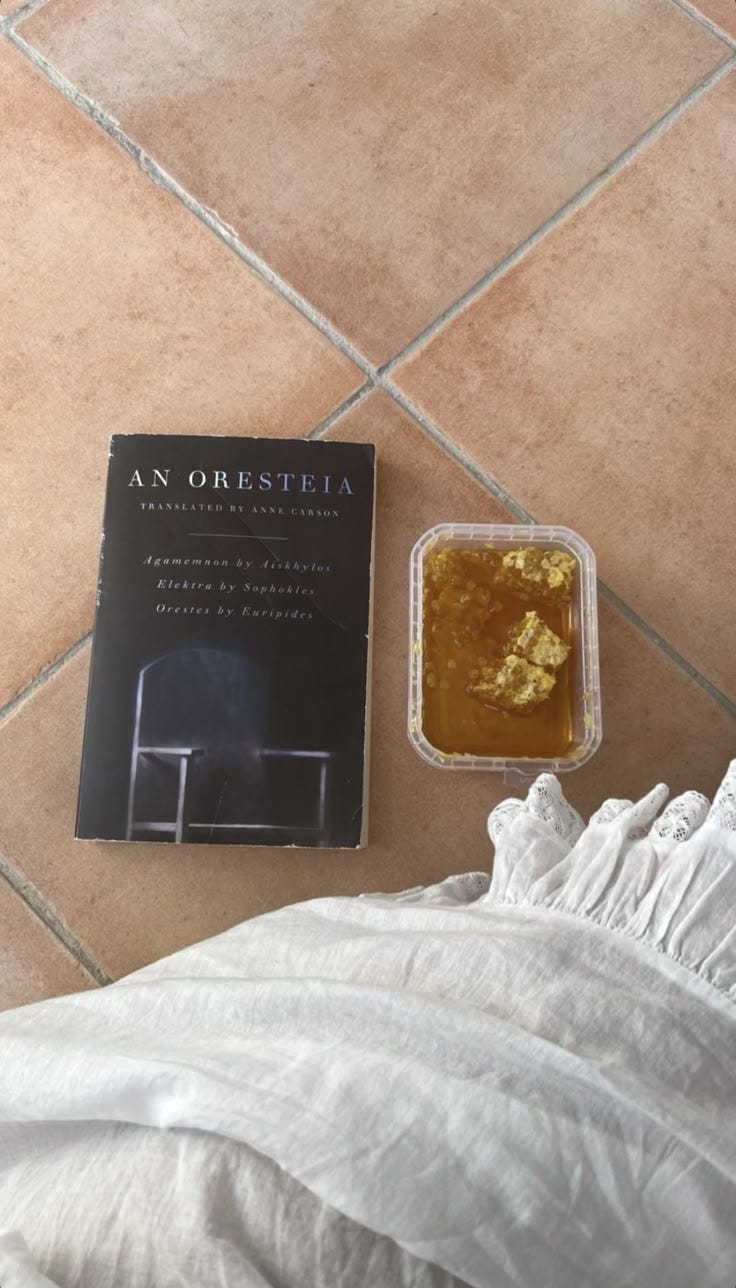 This may contain: an open book sitting on top of a bed next to a bowl of food and a plastic container