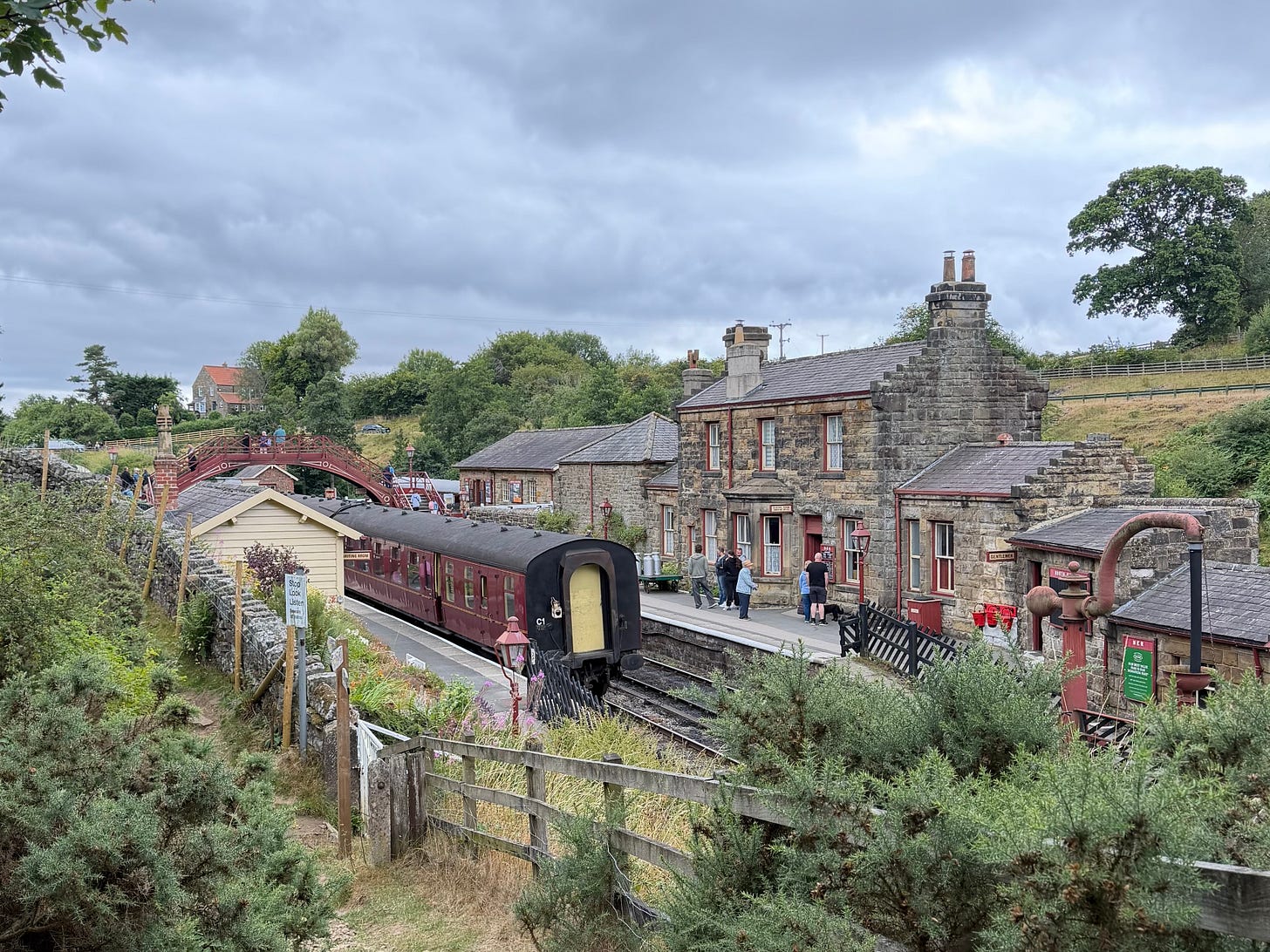 Goathland Station with a heritage train beside the platform and stone station buildings.