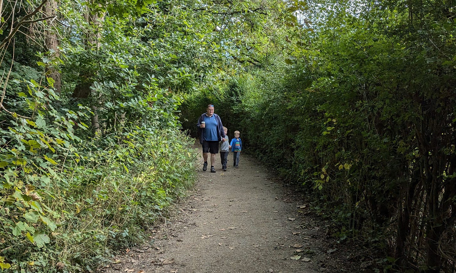 A tall, large man (Andrew) with his two young boys, walking on a path with greenery around it