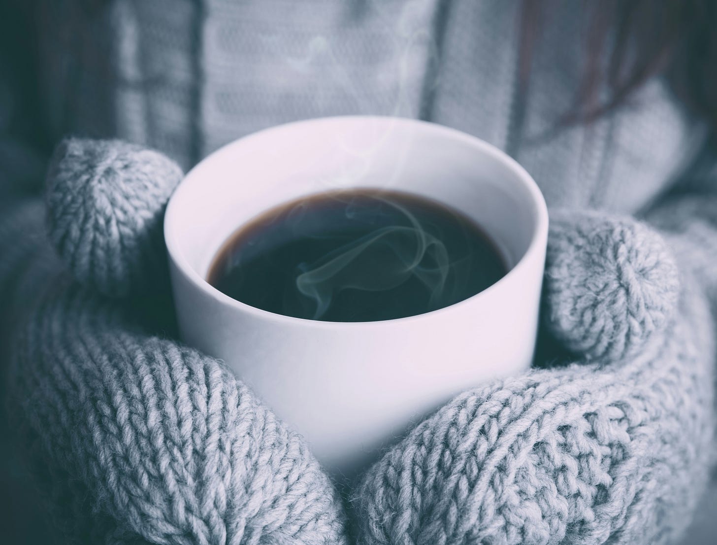 Image of mittened hands holding a mug of coffee. 