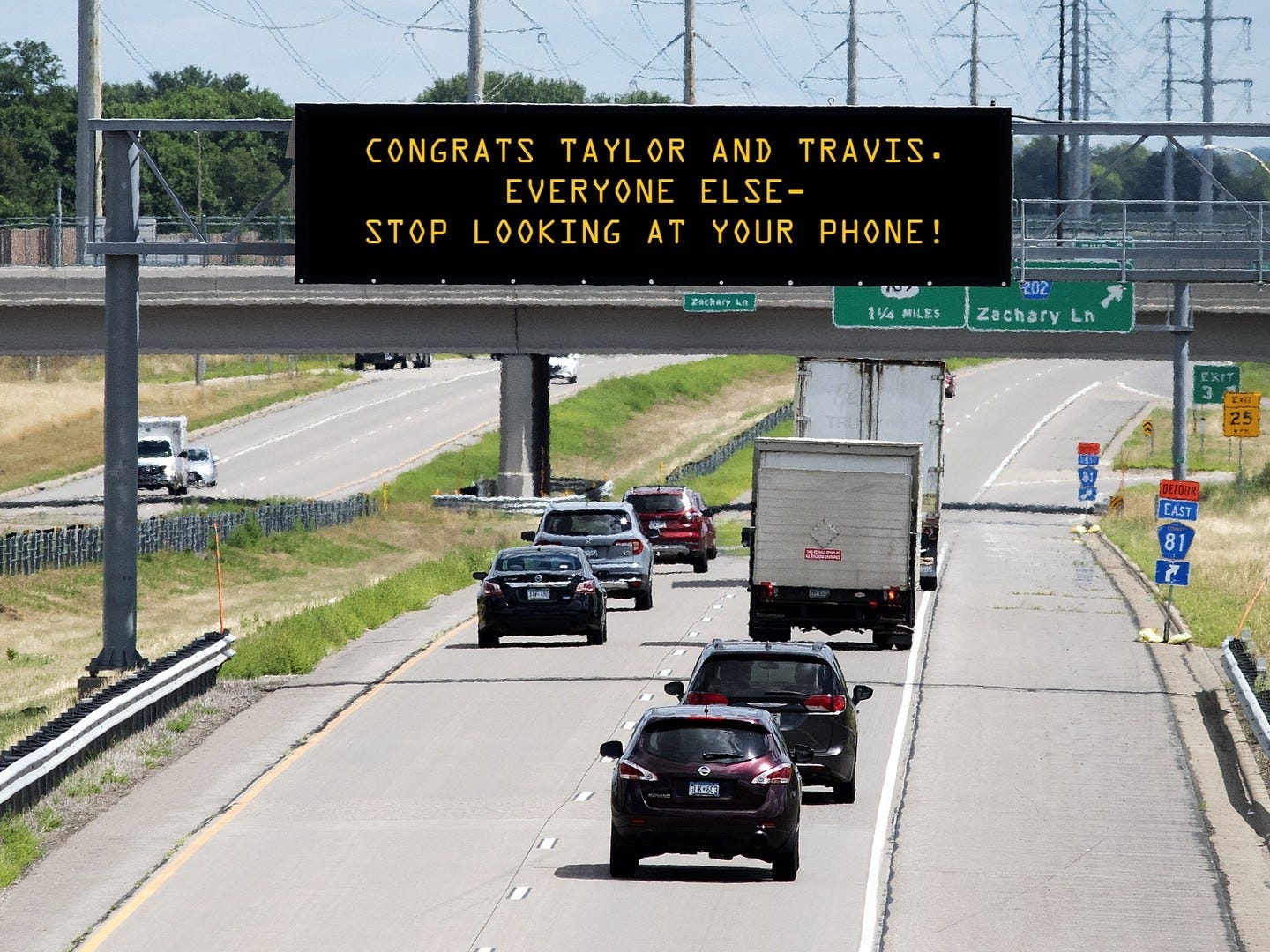 Highway scene with various cars and a bridge overhead displaying a digital sign that reads, "Congrats Taylor and Travis. Everyone else--stop looking at your phone!"