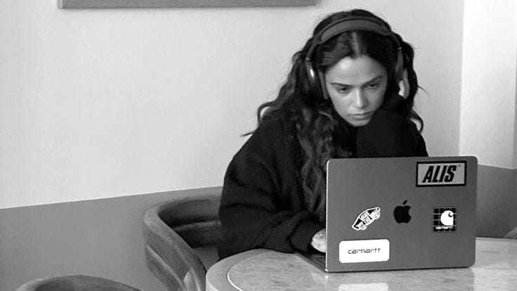 This may contain: a woman sitting at a table with a laptop computer in her hand and headphones on