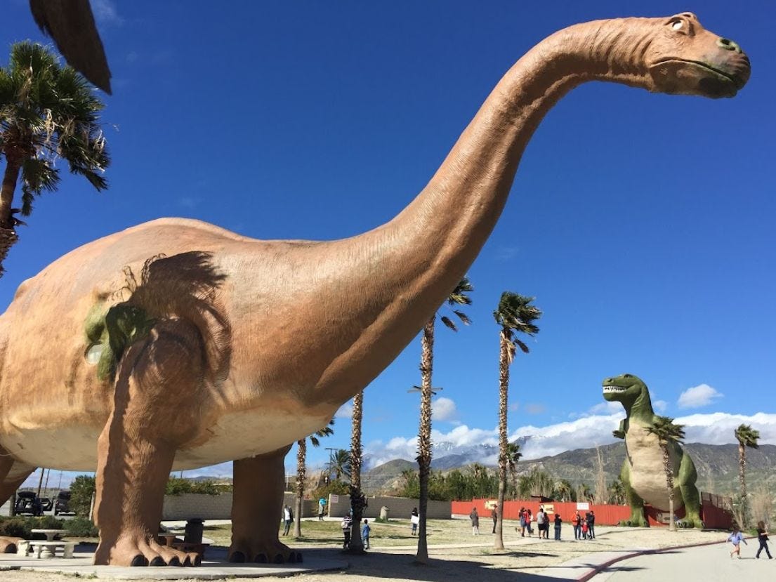 Image: Two "life-sized" fabricated dinosaurs at a tourist attraction in the desert.