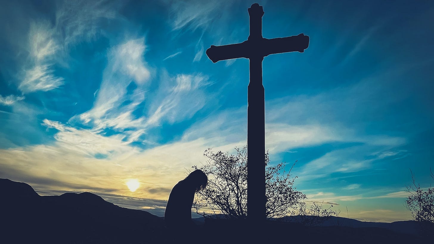 Image of person kneeling at a cross outdoors.