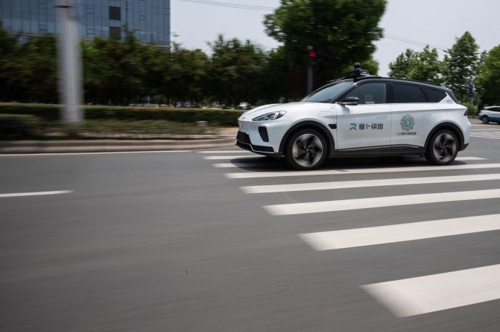 A white Baidu Apollo RT6 robotaxi moving on a road with a crosswalk.
