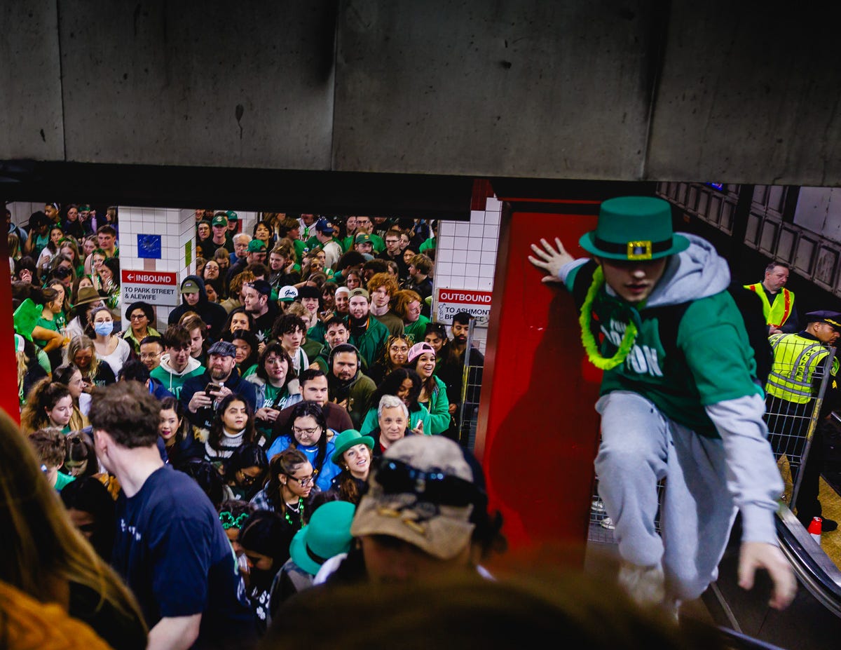 Large crowd of people in green fills a subway station during St. Patrick’s Day, with one person dressed as a leprechaun climbing over an escalator barrier. Large crowd of people in green fills a subway station during St. Patrick’s Day, with one person dressed as a leprechaun climbing over an escalator barrier.